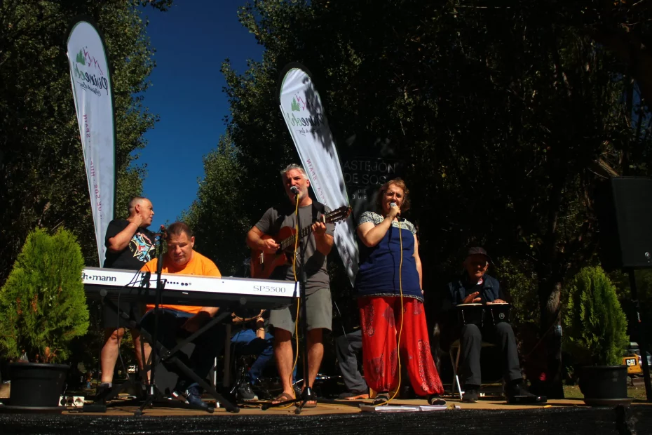 Imagen de un concierto de La Remós Band Se ven, de izquierda a derecha, a Sergio, a Aniano, sentado frente a su organo, a Pablo, con una guitarra y cantando, a Isabel, cantando con un microfono, y a Ernesto, sentado tocando los bongos. Están sobre un escenario en mitad de un parque. Es un dia soleado.