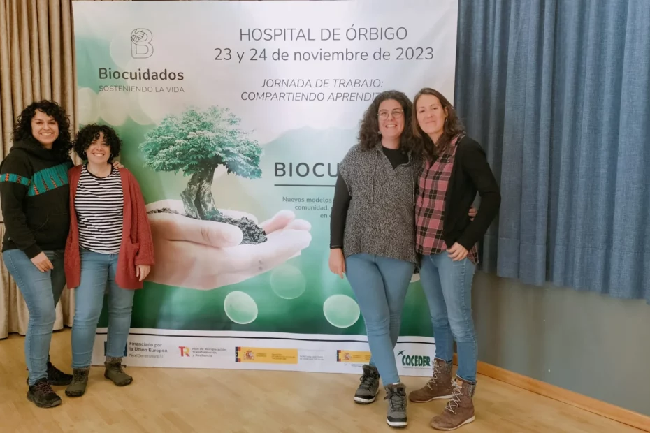 Cuatro técnicas del CDR Guayente posan ante el cartel del encuentro de entidades que realizan el programa Biocuidados celebrado en Hospital de Órbigo, en la provincia de León