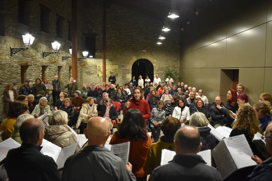 Miembros del coro Santo Domingo intepretan, dando la espalda a la cámara, una pieza bajo la dirección de su profesora. AL fondo aparece el público en el patio interior del Palacio de los Condes de Ribagorza de Benasque.