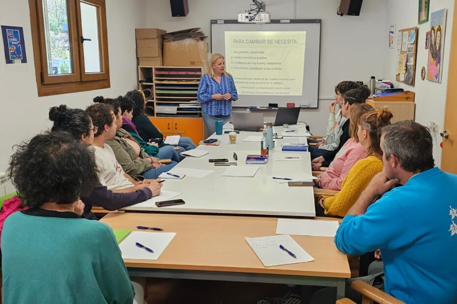 Formación en El Remós sobre la Atención Integrada y Centrada en la Persona. En la foto aparece Maica, la ponente, delante de una pantalla en la que se proyecta un contenido del curso, mientras que los trabajadores de El REmós están sentados alrededor de una mesa, atendiendo a la formación.